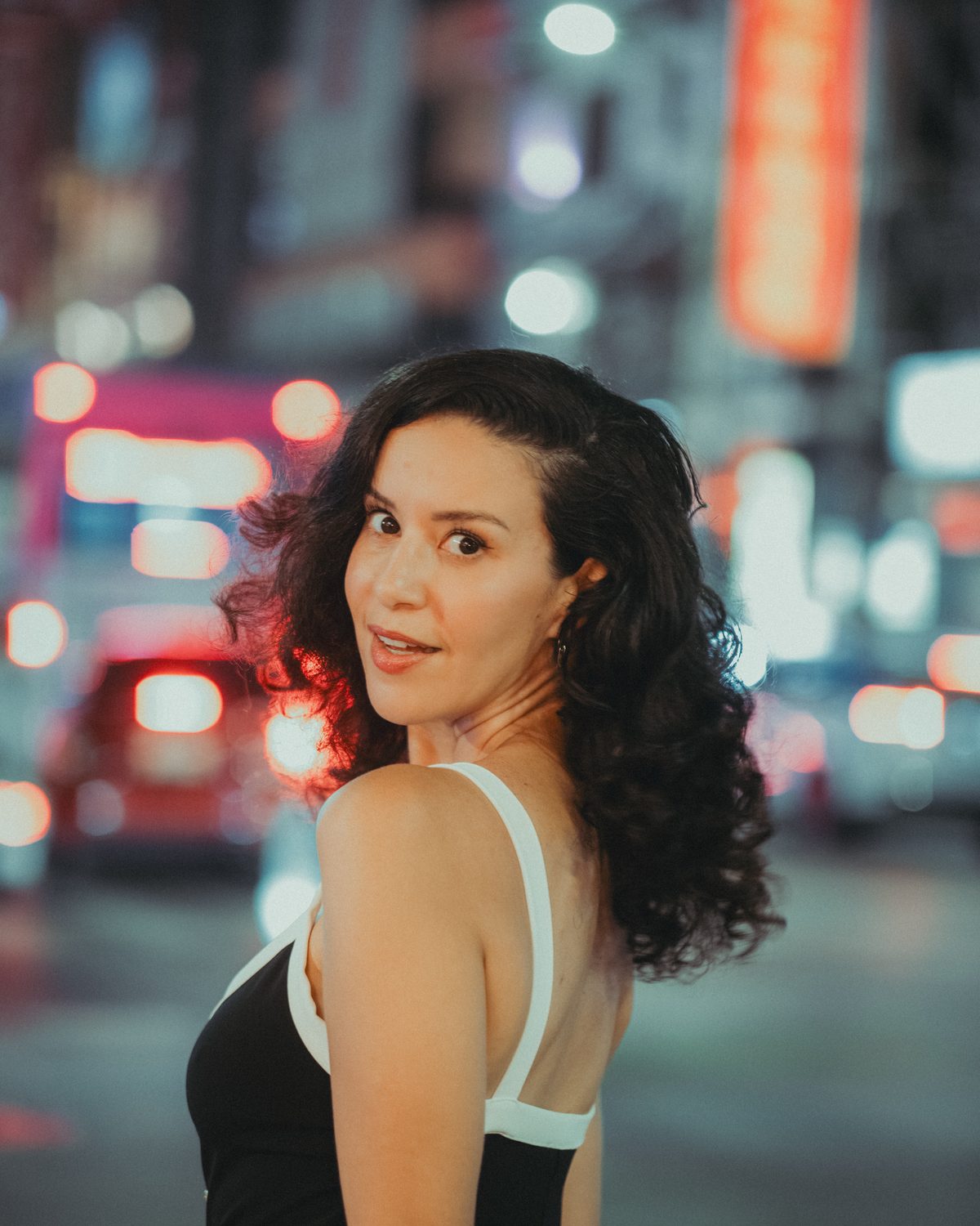 Amelle Zaïd se retourne vers l’objectif, le soir, dans une rue de Bangkok illuminée de néons.