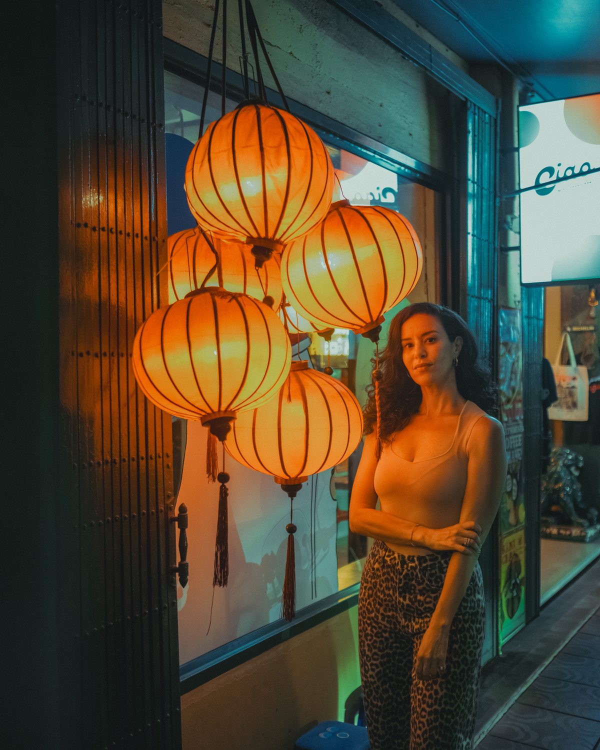Amelle pose le soir à côté de grandes lanternes orange, devant une vitrine de Bangkok.